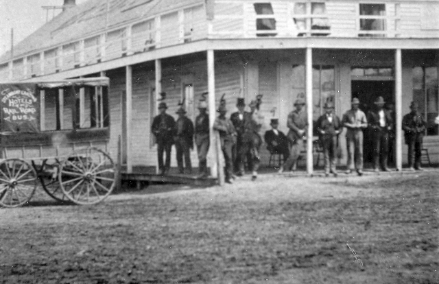 Men standing on porch of Merchants Hotel 1876